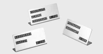 Minimalist stainless steel price tags on a wooden counter in a modern café setting