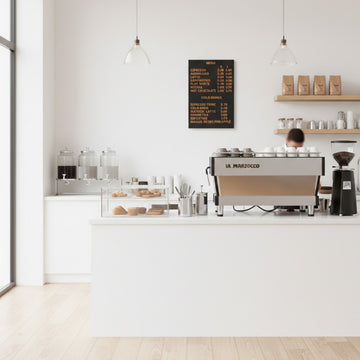 Magnetic black menu board displayed in a modern minimalist café interior with wooden shelves and espresso machine.